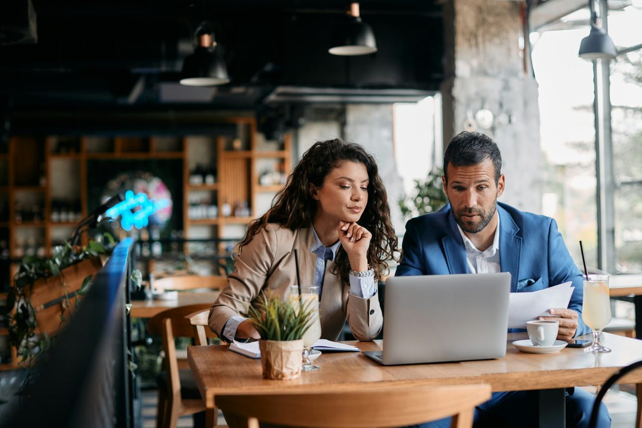 business-colleagues-using-laptop-and-analyzing-documents-on-a-meeting-in-cafe